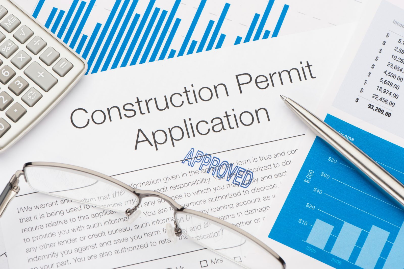 A stamped construction permit application with calculator, glasses and summary charts.